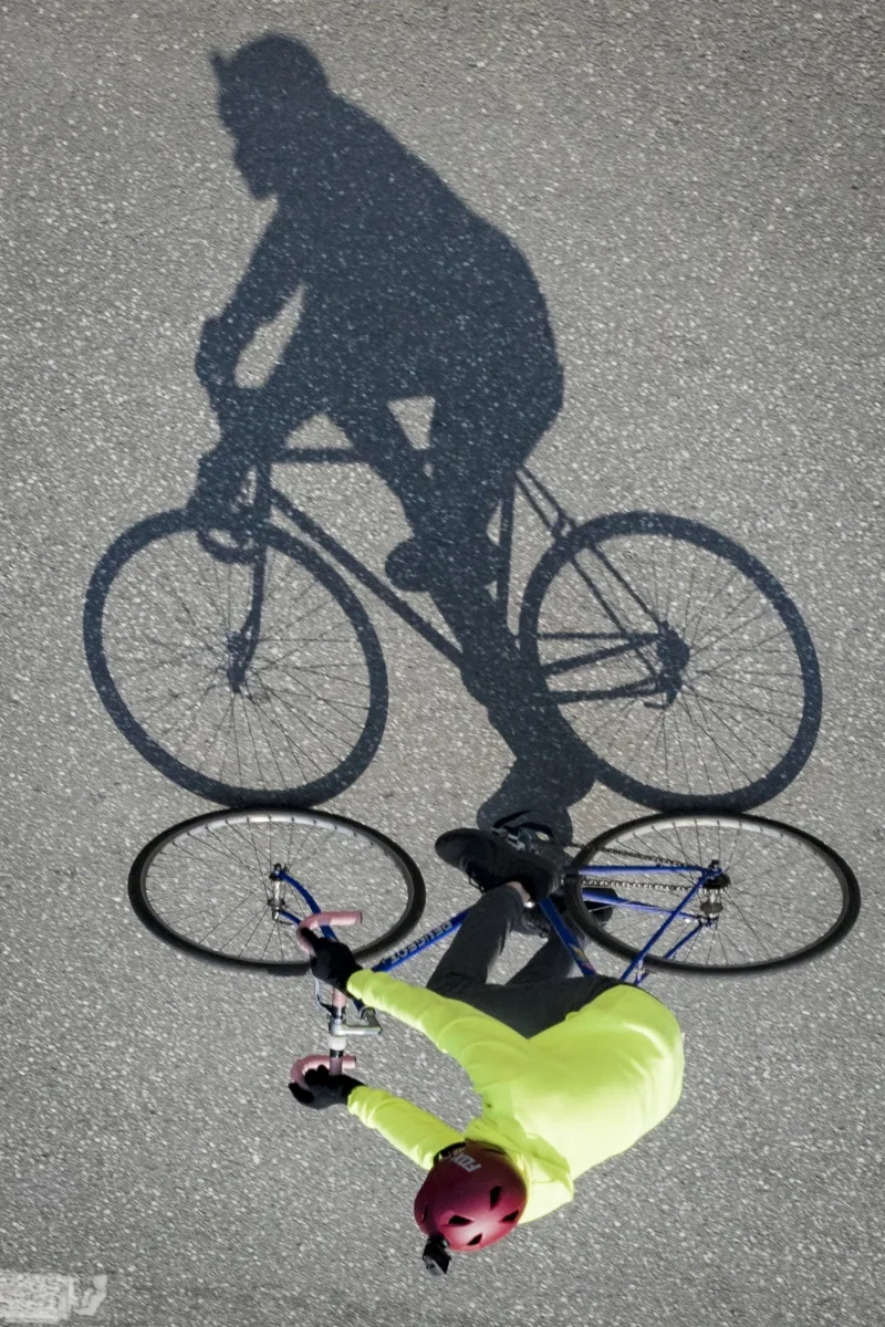 Shadow of a cyclist passing beside a bright green bicycle seat